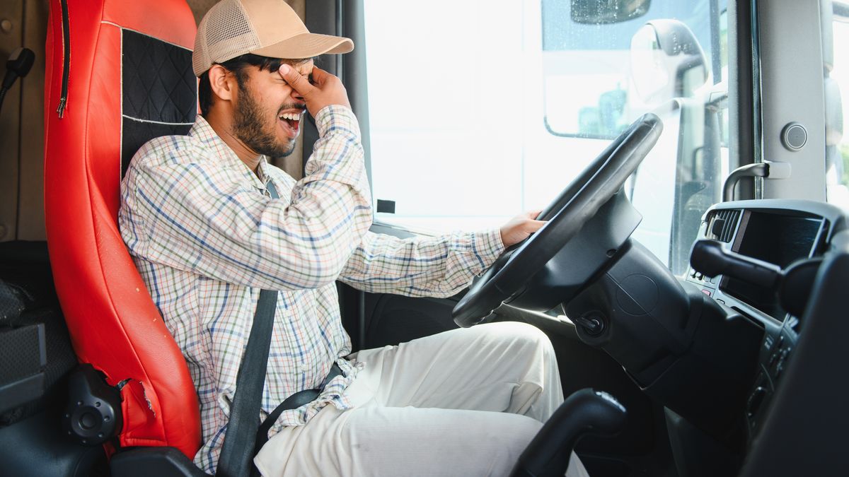 A worried truck driver rubbing his eyes in the cab
