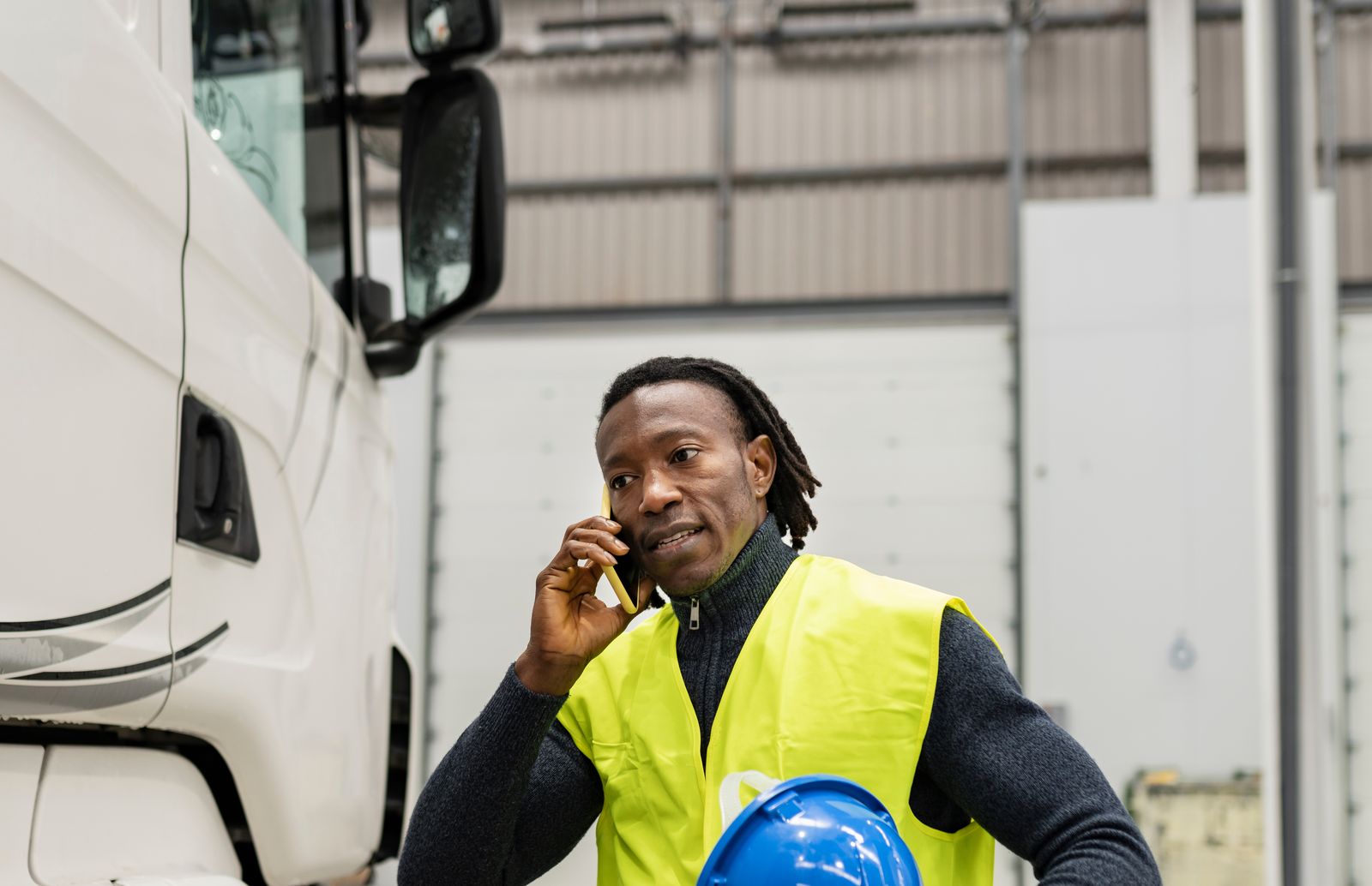 A truck driver in a hi-vis vest takes a difficult phone call beside his trailer